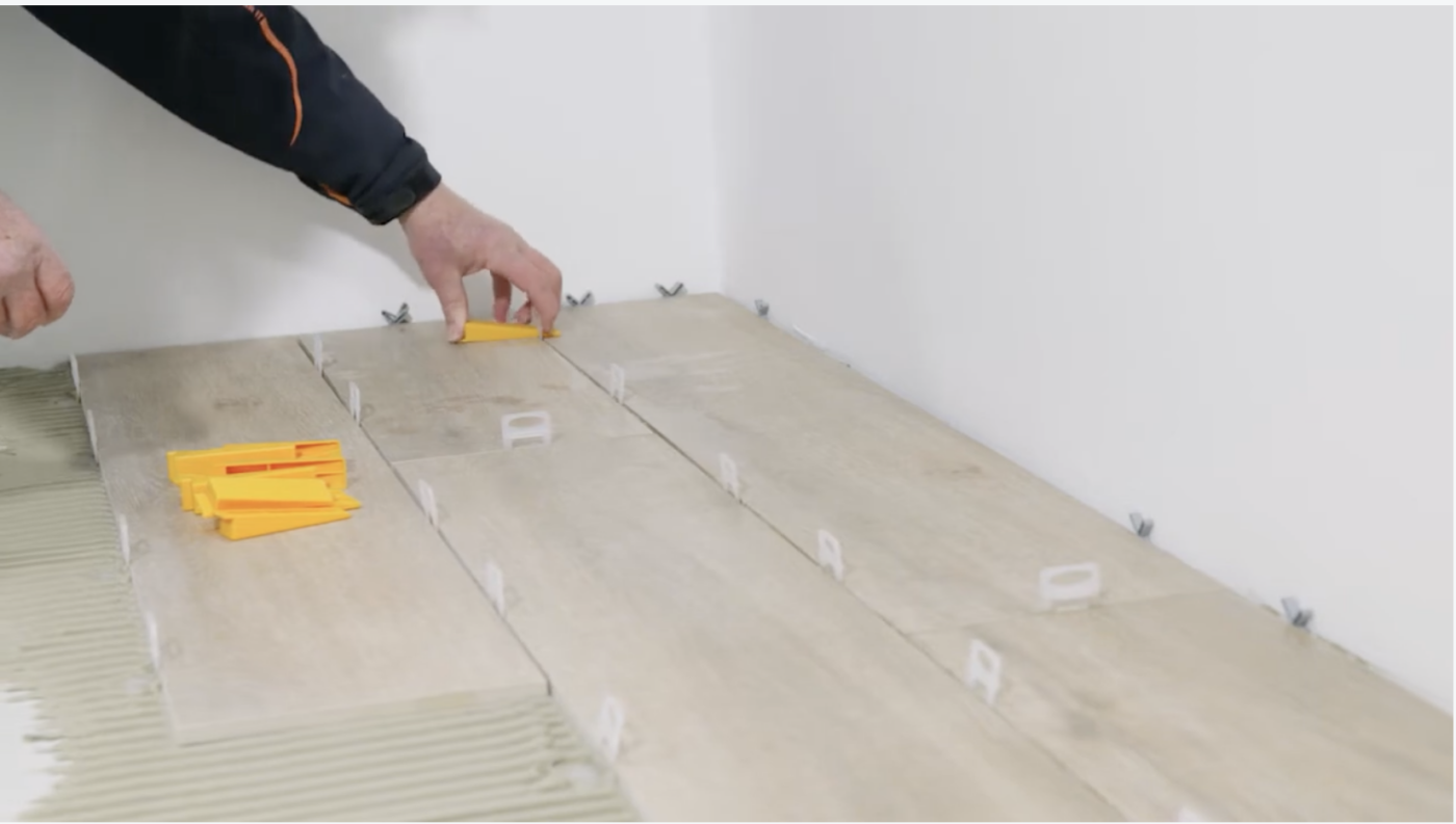 Tegelzetter die de spieen door de clips van het leveling systeem schuift.