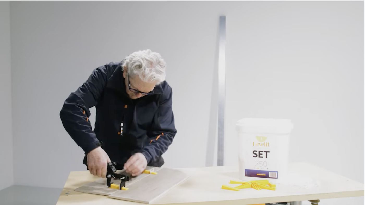 Tegelzetter die de plastic instelbare tegeltang instelt op het leveling systeem.