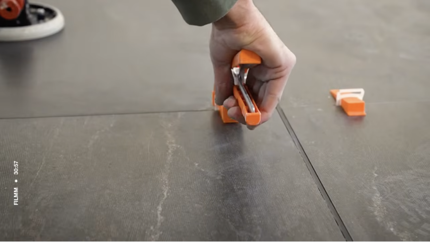 Tegelzetter spant een Levelit nivelleerspie aan met een fixeertang.